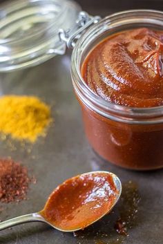 two spoons filled with sauce and spices on top of a metal surface next to a jar