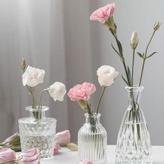 three clear vases with pink and white flowers in them sitting on a table top