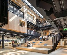 people are sitting on the stairs in an open area with large windows and wooden staircases