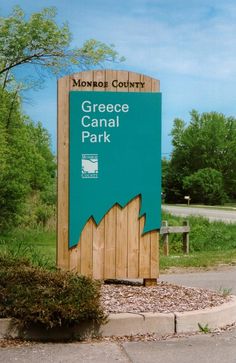 a wooden sign sitting on the side of a road next to a lush green field