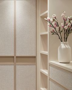 a vase filled with flowers sitting on top of a white shelf next to a bookcase