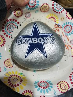 someone is holding a rock with the word cowboys on it in front of a flowered plate