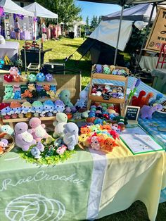 there are many stuffed animals on display at this outdoor market table with umbrellas in the background