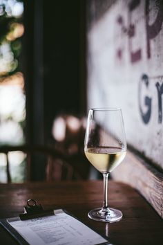 a glass of white wine sitting on top of a wooden table next to a menu