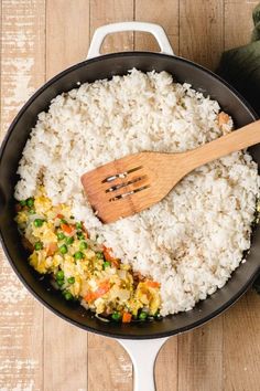 rice and vegetables being cooked in a skillet with a wooden spatula on the side