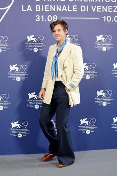 a man standing in front of a blue wall wearing a suit and tie with his hands in his pockets