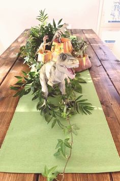 a dinosaur statue sitting on top of a wooden table next to plants and potted plants