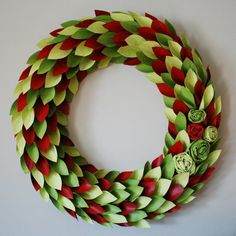 a wreath made out of green, red and yellow paper flowers on a wall with a white background