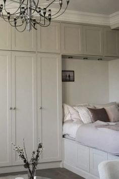 a bedroom with white furniture and a chandelier hanging from the ceiling over a bed