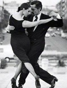 a man and woman dance together on the sidewalk in black and white, with their arms around each other