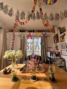 a table with wine glasses, plates and flowers on it in front of a window