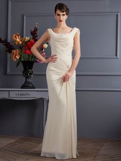 a woman in a white dress standing next to a vase with flowers on the table