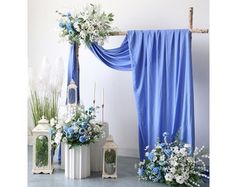 blue and white flowers are on display in front of an arch decorated with draping