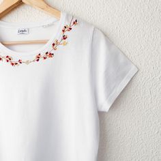 a white t - shirt with red and yellow flowers hanging on a wooden hanger