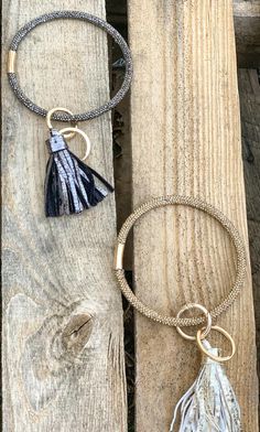 two bracelets with tassels are on a piece of wood and one is hanging from it