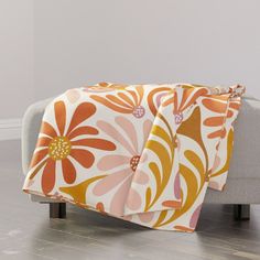 an orange and white flowered blanket sitting on top of a gray couch in a living room