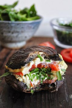 an open faced sandwich on a wooden table with tomatoes and other food items in the background