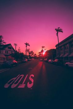 the sun is setting on an empty street with palm trees in the foreground and pink sky