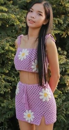 a young woman standing in front of trees wearing a purple outfit with white flowers on it