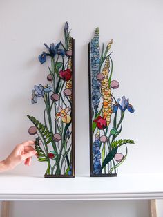 two pieces of art made out of paper with flowers and plants painted on the sides