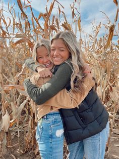 two girls hugging each other in front of a corn field