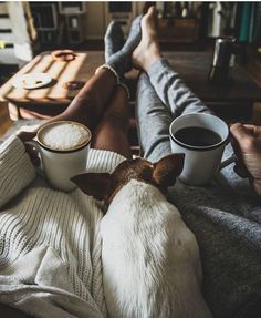 a dog sitting on top of a couch next to two people holding coffee mugs