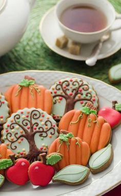 decorated cookies are on a plate next to a cup of tea