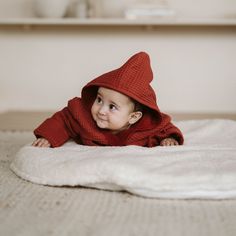 a small child laying on top of a bed wearing a red sweater and hoodie