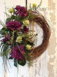 a wreath with flowers hanging on a door