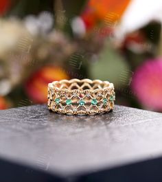 a gold ring with emeralds and diamonds sitting on top of a wooden table in front of flowers