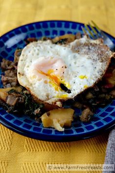 a blue plate topped with an egg on top of potatoes and meat next to a fork