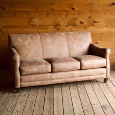 a tan couch sitting on top of a wooden floor next to a wood paneled wall