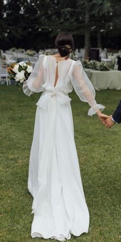 a bride and groom hold hands as they walk through the grass