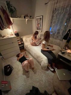 three women sitting on a bed in a room with two laptops and other items