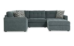 a gray sectional couch with pillows on the top and bottom corner, in front of a white background