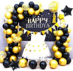 a black and gold happy birthday balloon arch with stars, balloons and a white dress