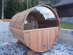 a wooden barrel sauna sitting on top of a stone floor next to a building