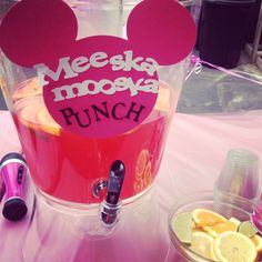 a pink table topped with a cup filled with liquid and lemon wedges next to a bowl of orange slices