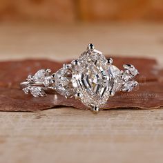 an engagement ring with three pear shaped diamonds on top and leaves in the bottom, sitting on a piece of wood