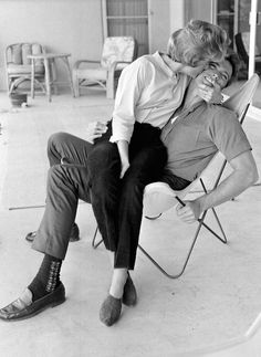 a man and woman sitting in lawn chairs with their faces close to each other as they kiss