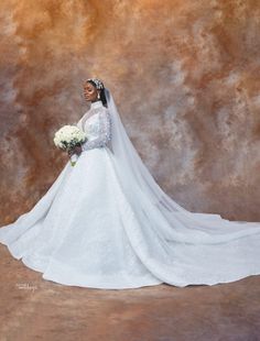 a woman in a white wedding dress holding a bouquet and posing for a photo with a brown background