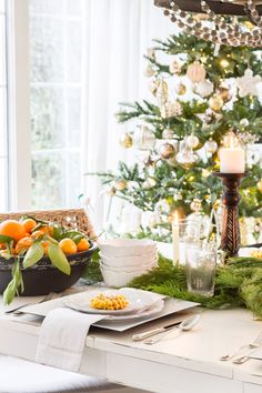 a christmas table setting with oranges, corn and candles on the table in front of a decorated christmas tree