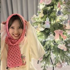 a young woman wearing a pink scarf next to a christmas tree with ornaments on it