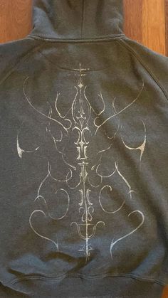 the back of a hoodie with an intricate design on it sitting on a wooden floor