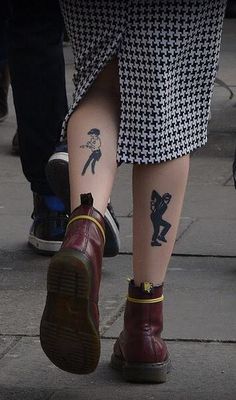 two people with tattoos on their legs walking down the street, one wearing red boots