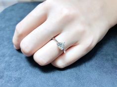 a woman's hand with a diamond ring on top of her finger, sitting on a blue surface