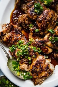 a white plate topped with meat covered in sauce and garnished with green onions