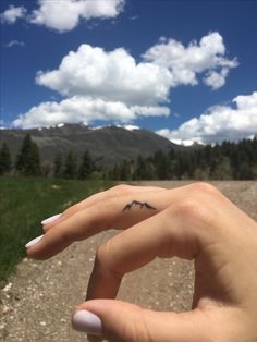 a person's hand with a small tattoo on their left thumb and the sky in the background