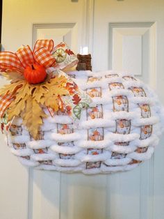 a white pumpkin shaped door hanger decorated with fall leaves and plaid fabric, hanging from a front door