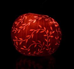 a pumpkin decorated with vines and leaves on a black background, lit up in the dark